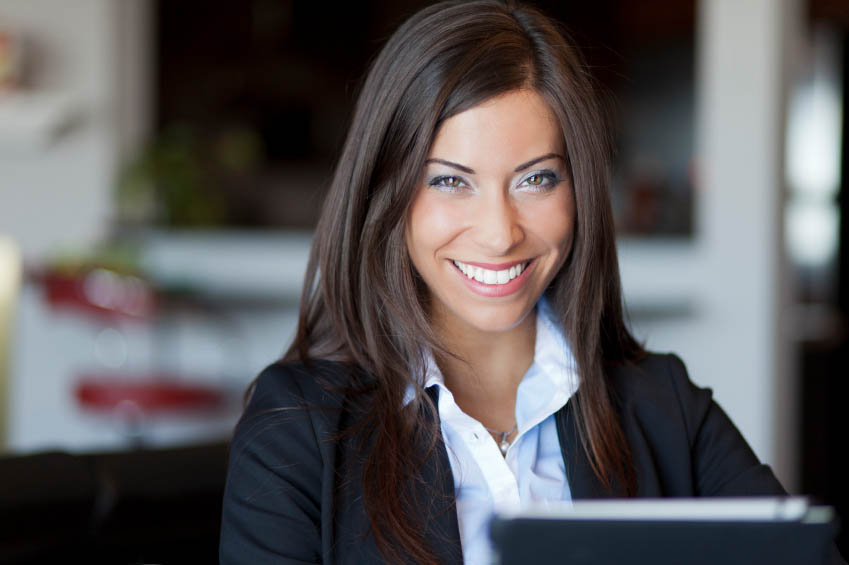 A woman in a business suit smiles at the camera in a professional setting.