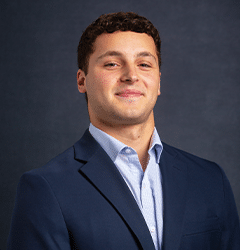 Mujer sonriente con cabello largo y oscuro, vestida con una blusa blanca y una chaqueta negra sobre un fondo blanco liso.